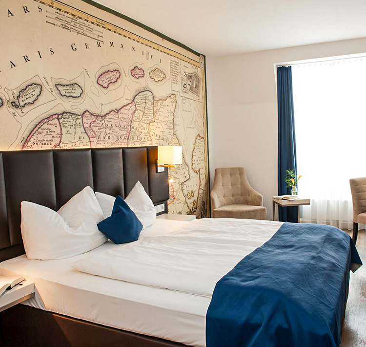 Hotelzimmer mit einem Bett, einem Sessel und einer Landkarte an der Wand.