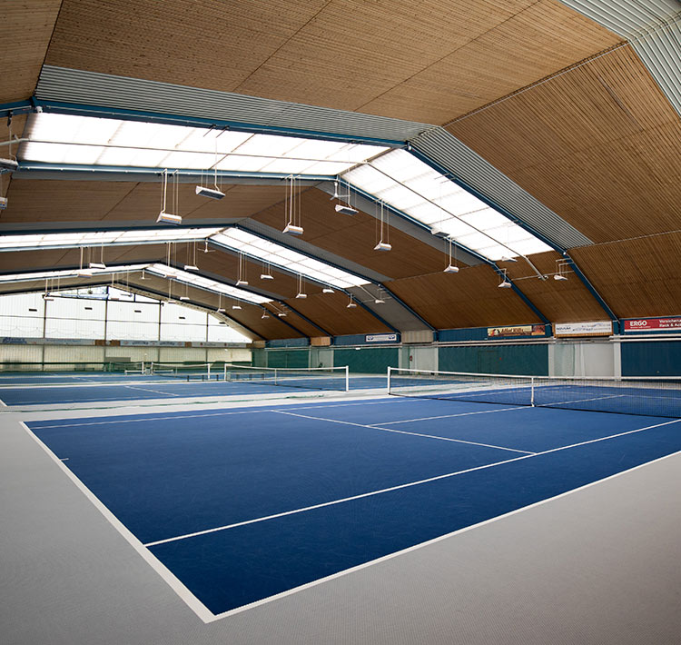 Sporthalle mit drei blauen Tennisfeldern.