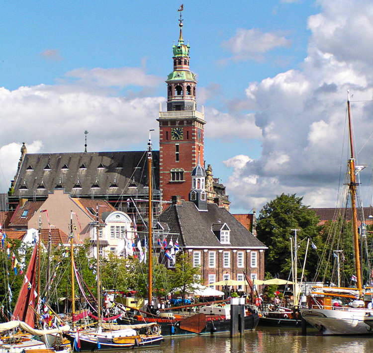 Hafen mit Booten vor Backsteinhäusern und einer Kirche.