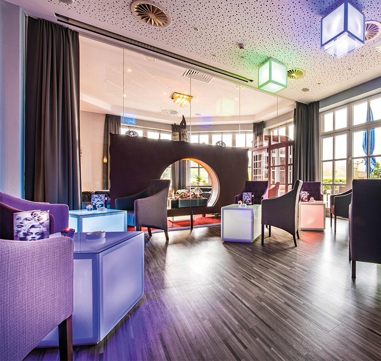 Moderne Lounge mit Sesseln, Leuchtwürfel-Tischen und Leuchtwürfel-Deckenlampen.