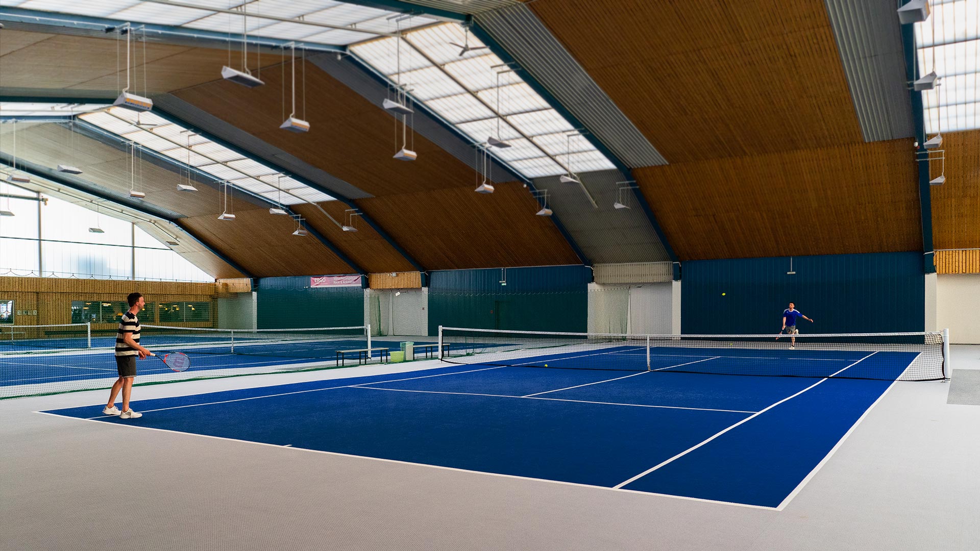 Zwei Tennisspieler in einer Sporthalle auf einem blauen Tennisplatz.