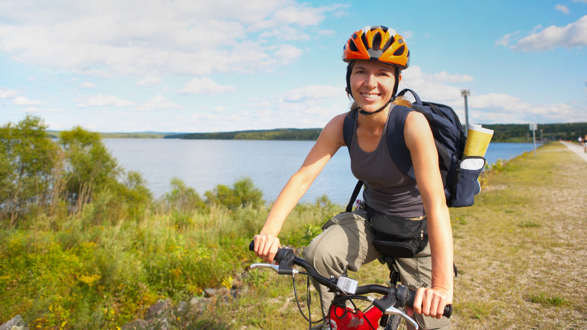 Nahaufnahme einer Fahrradfahrerin mit Helm vor einem Gewässer.