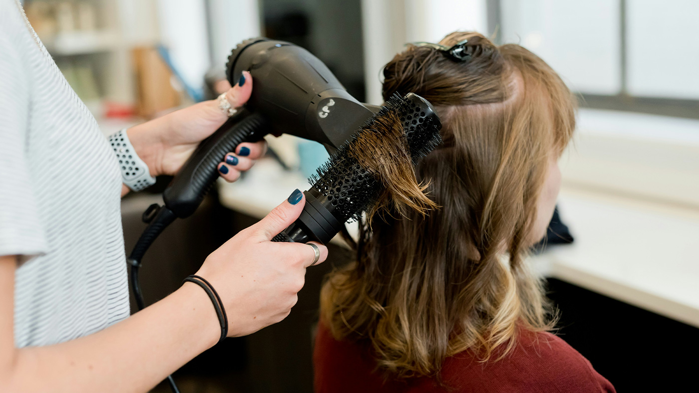 Nahaufnahme eines Föhns und einer Bürste beim Stylen von Haaren.