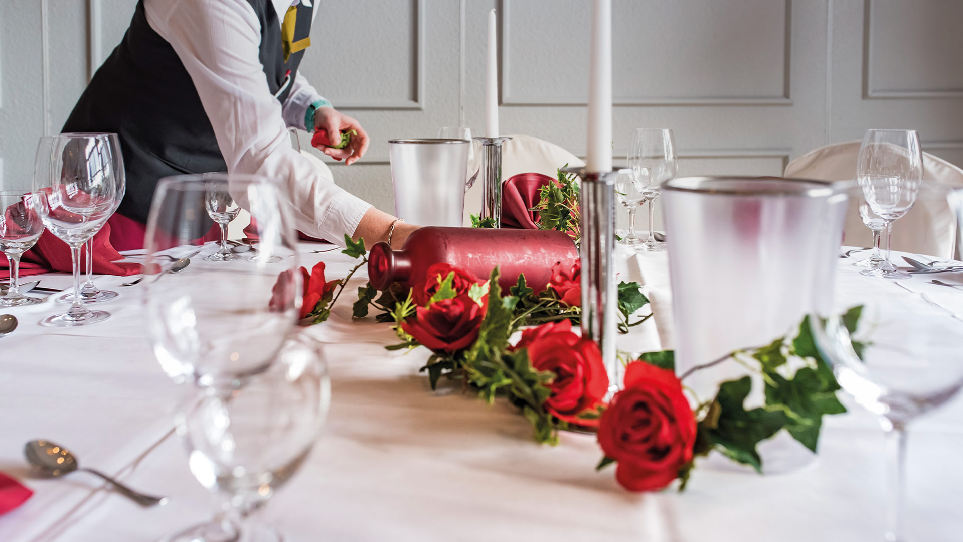 Nahaufnahme eines gedeckten Tisches mit weißer Tischdecke und roten Rosen.
