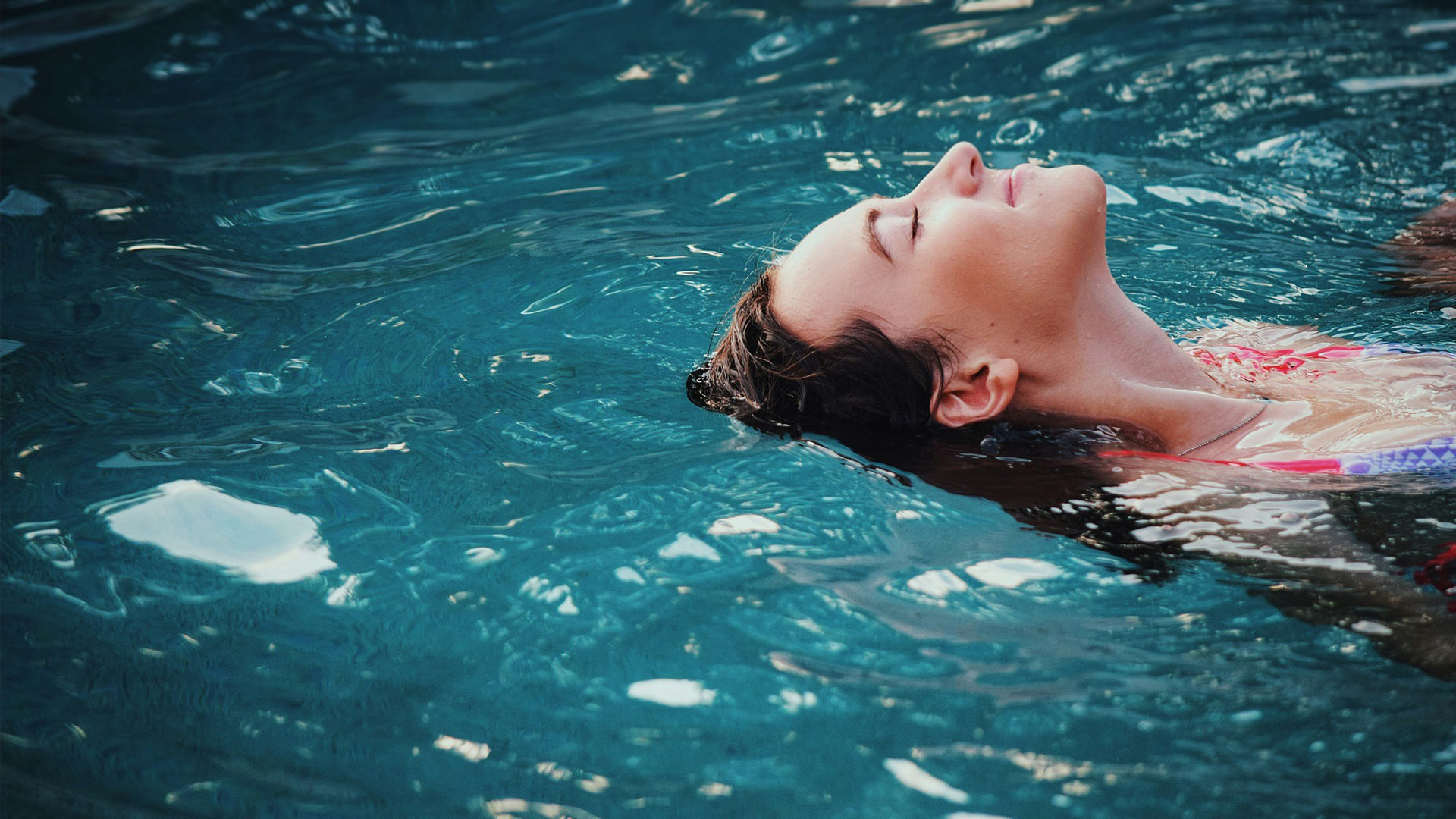 Nahaufnahme einer Frau, die im Wasser eines Pools liegt.