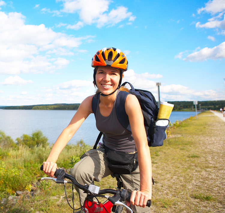 Nahaufnahme einer Fahrradfahrerin mit Helm vor einem Gewässer.