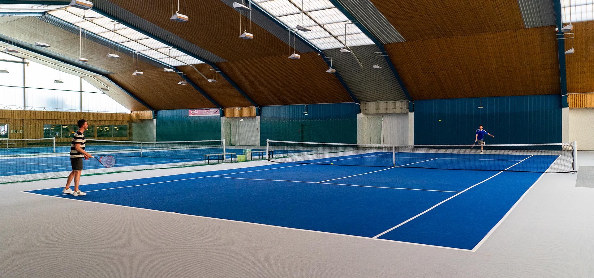 Zwei Tennisspieler in einer Sporthalle auf einem blauen Tennisplatz.