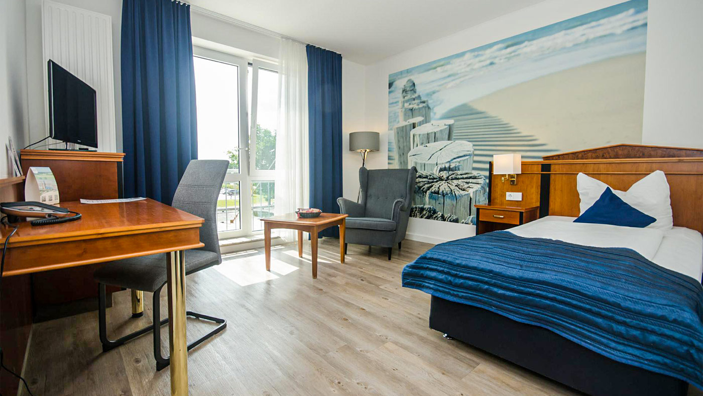 Hotelzimmer mit Bett, Schreibtisch, Lampe und Wandbild.
