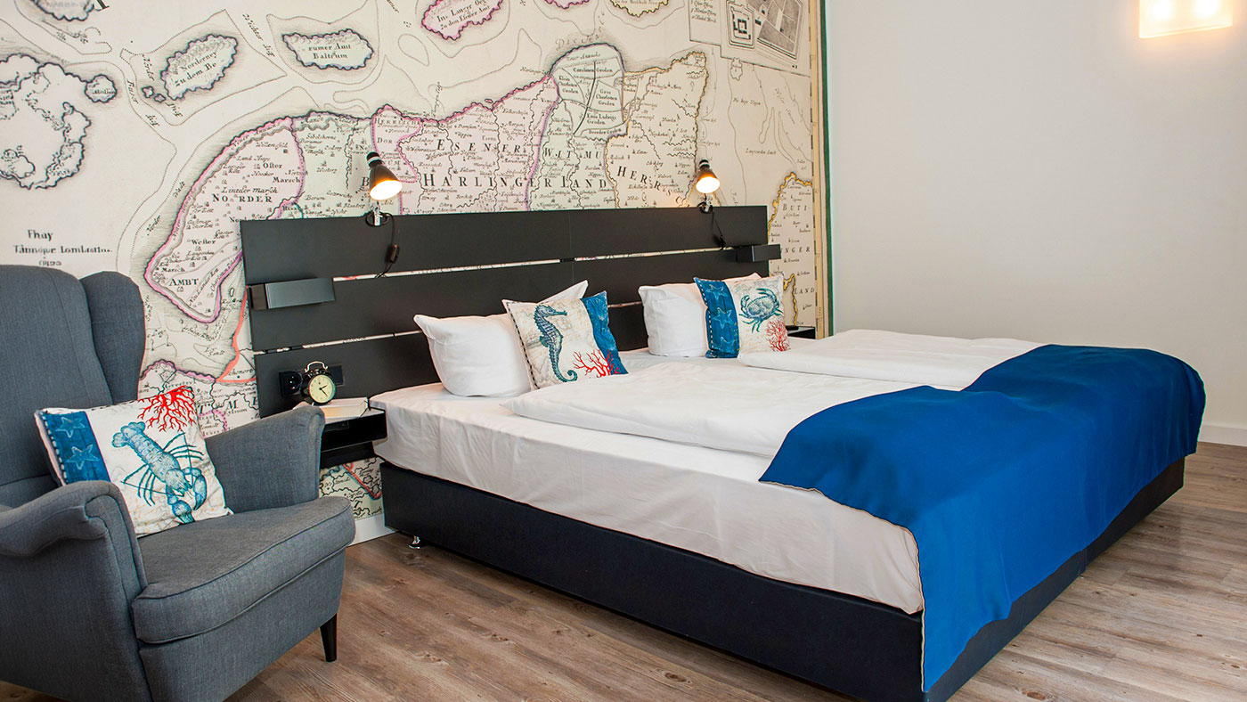Nahaufnahme eines Hotelzimmers mit Bett, Sessel und Landkarte an der Wand.