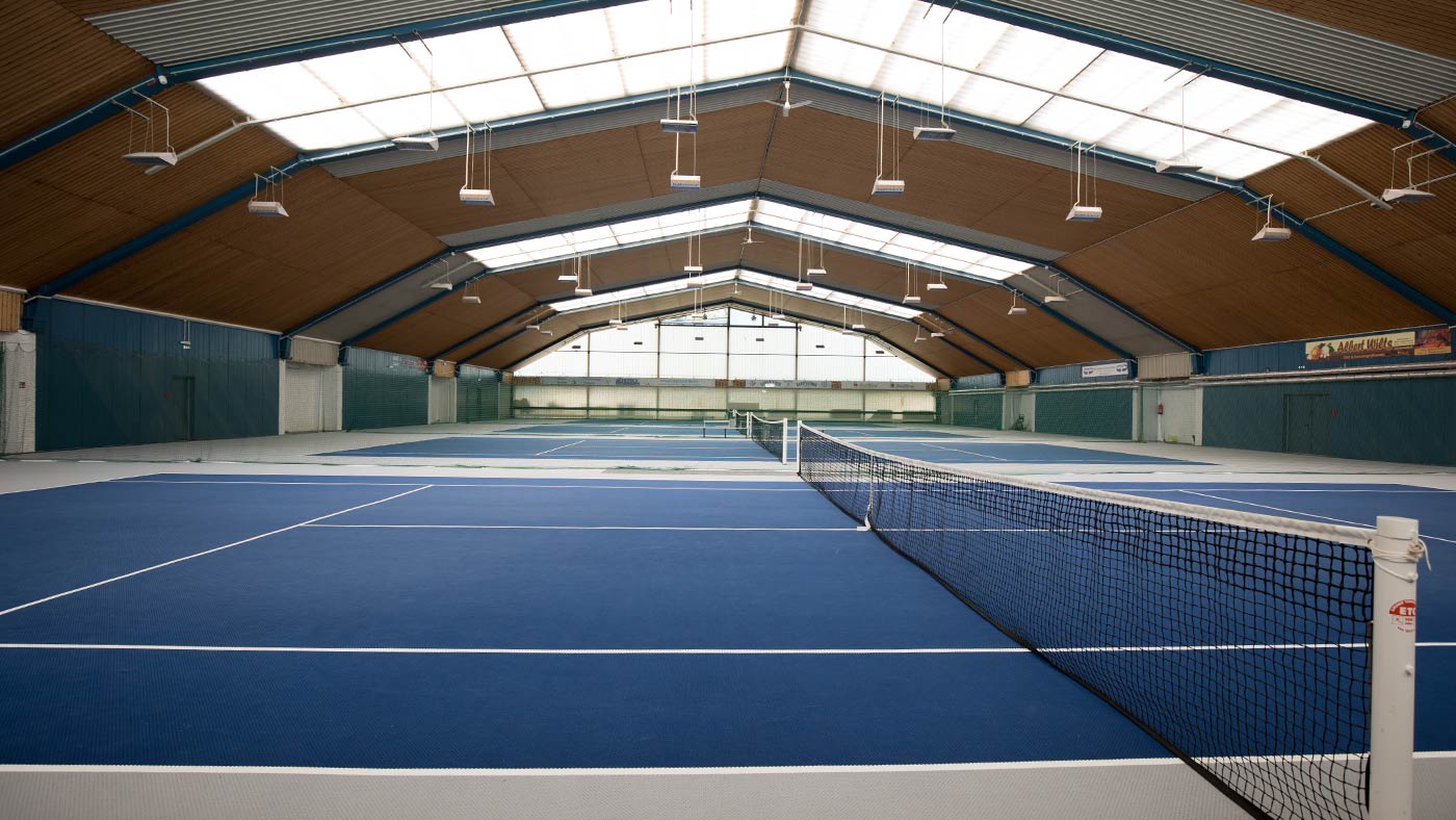 Sporthalle mit drei blauen Tennisfeldern.